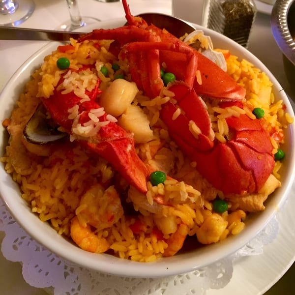 A large bowl of Portuguese seafood paella with lobster, shrimp, clams, and rice.