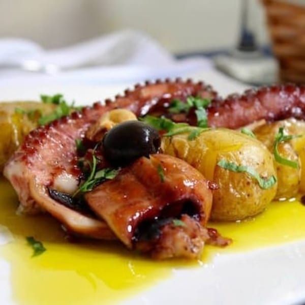 Portuguese grilled octopus with roasted potatoes, black olives, and fresh parsley, drizzled with olive oil.
