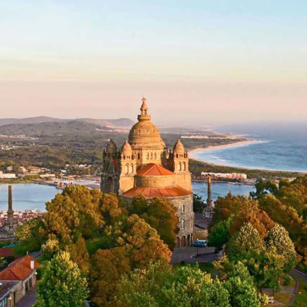 A Portuguese church with a large dome and red roofs, overlooking a river and coastline at sunset.