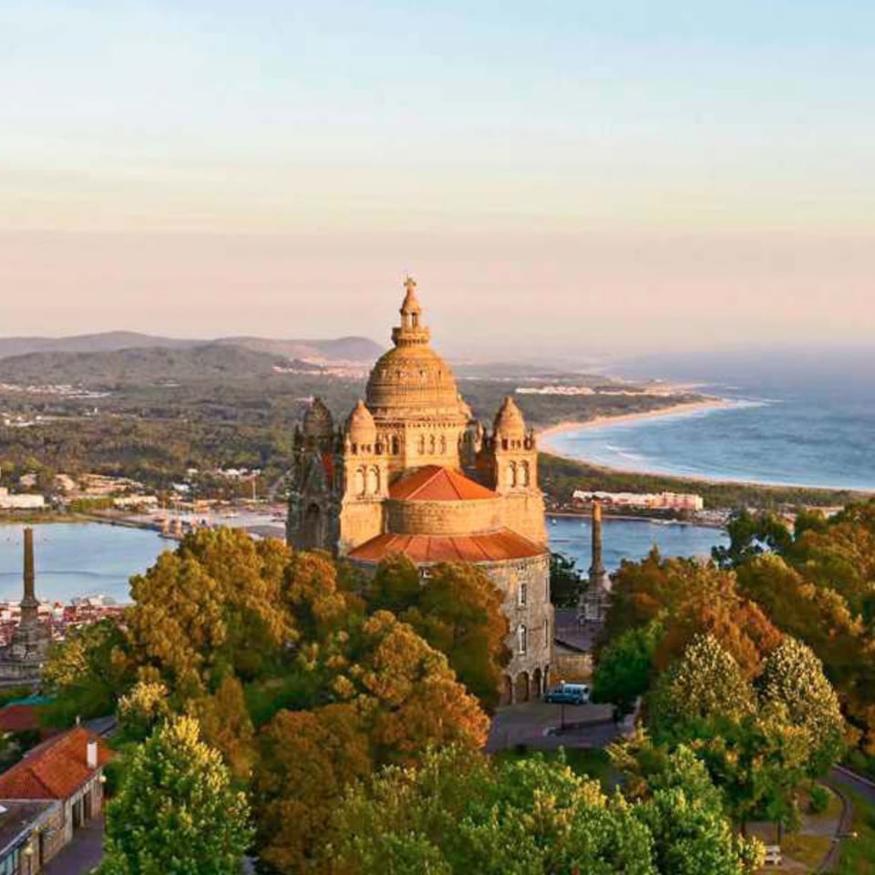 A Portuguese church with a large dome and red roofs, overlooking a river and coastline at sunset.