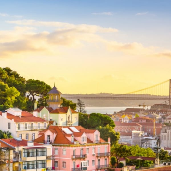 Panoramic view of Lisbon's colorful buildings and the 25 de Abril Bridge at sunset.