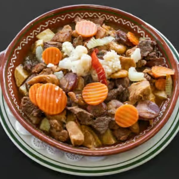Hearty Portuguese stew with meat, potatoes, carrots, and cauliflower in a rustic bowl.