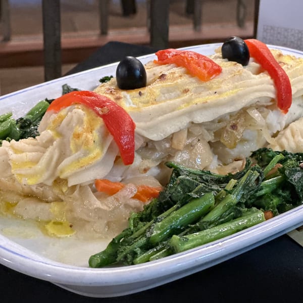 Portuguese Bacalhau à Brás with shredded cod, onions, potatoes, olives, and red peppers, served with greens.