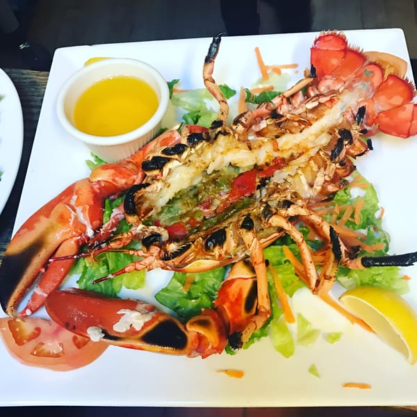 Grilled lobster, split open, served with a side of melted butter, lettuce, tomato, and lemon.